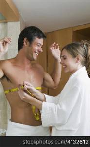 Young woman measuring a mid adult man&acute;s chest with a tape measure