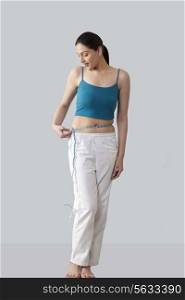 Young woman measuring waist isolated over gray background