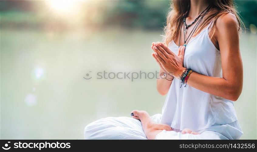 Young woman meditates, practicing yoga in nature. Sitting in lotus pose with hands in prayer position.