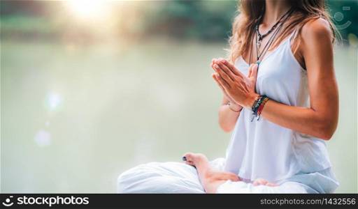 Young woman meditates, practicing yoga in nature. Sitting in lotus pose with hands in prayer position.