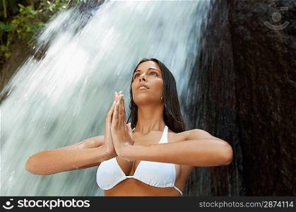 Young woman meditating by waterfall, low angle view