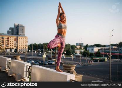 Young woman meditating in yoga pose, balance exercise, city on background. Yogi workout outdoors