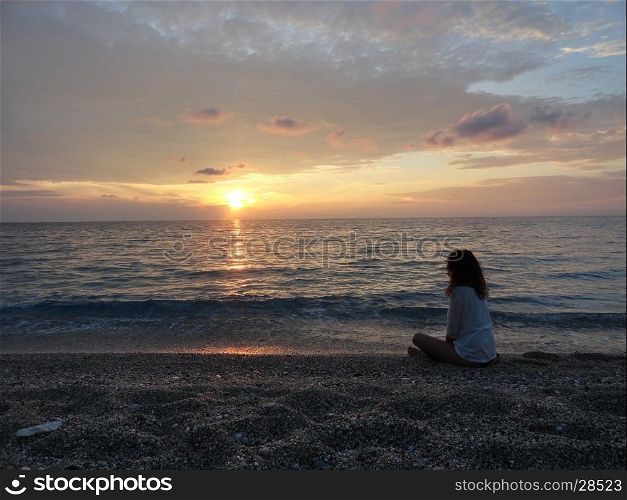young woman meditating on a greek beach at sunset