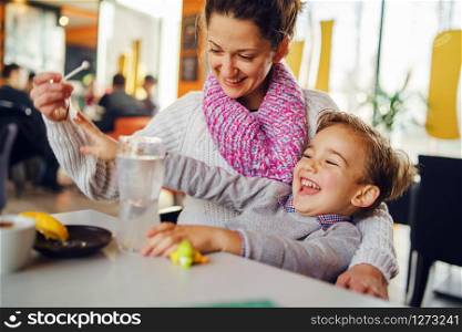 Young woman mother with small boy child son having fun at cafe or restaurant caucasian kid smiling while sitting by the table teasing playing