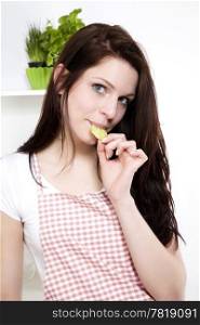 young woman nibbling on a cucumber. pretty young woman standing in her kitchen nibbling on a fresh cucumber