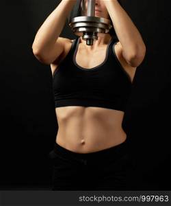 young woman of Caucasian appearance holds steel type-setting dumbbell in her hands, sports training, dark background