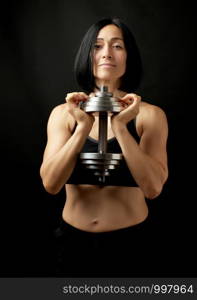 young woman of Caucasian appearance holds steel type-setting dumbbells in her hands, sports training, dark background