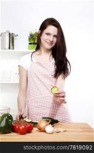 young woman offering a piece of cucumber. young happy woman in her kitchen offering a piece of cucumber