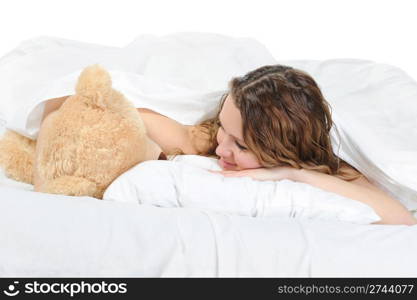 Young woman on a bed in an embrace with teddybear. Isolated on white background