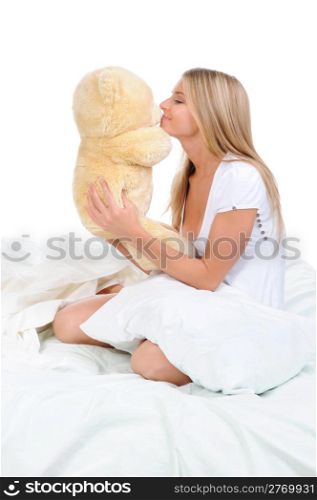 Young woman on a bed in an embrace with teddybear. Isolated on white background