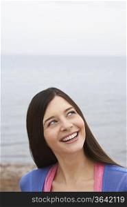 Young woman on beach, looking up and smiling
