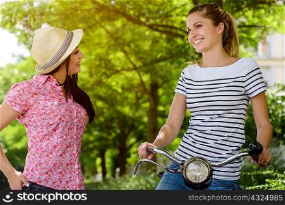Young woman on bicycle talking to young woman wearing panama hat