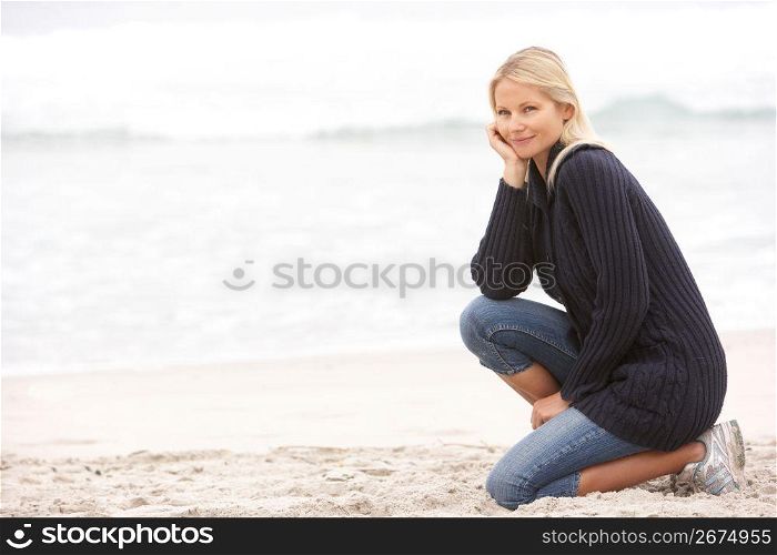 Young Woman On Holiday Kneeling On Winter Beach