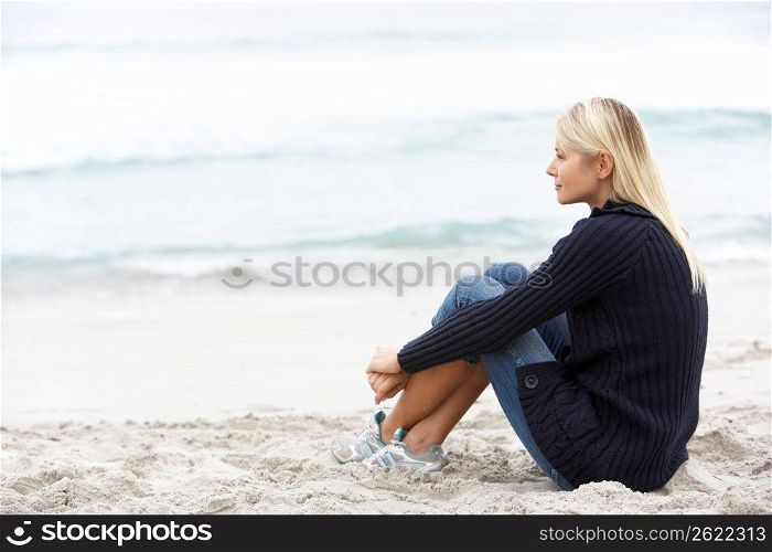 Young Woman On Holiday Sitting On Winter Beach