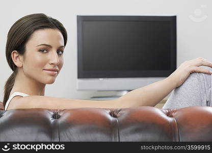 Young woman on sofa in front of flat screen television, portrait