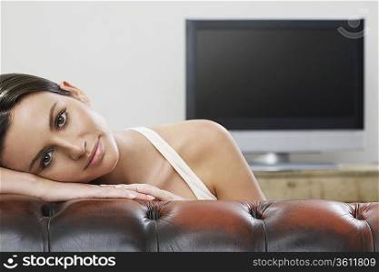 Young woman on sofa in front of flat screen television, portrait