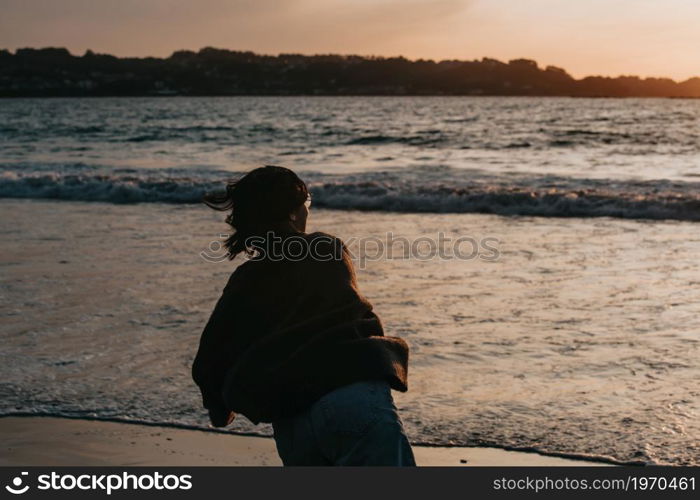 Young woman on spring clothes at the beach during a sunset throwing a rock to the ocean