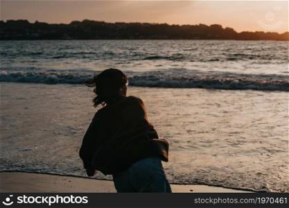 Young woman on spring clothes at the beach during a sunset throwing a rock to the ocean