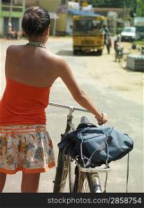 Young woman on street walking with bicycle back view