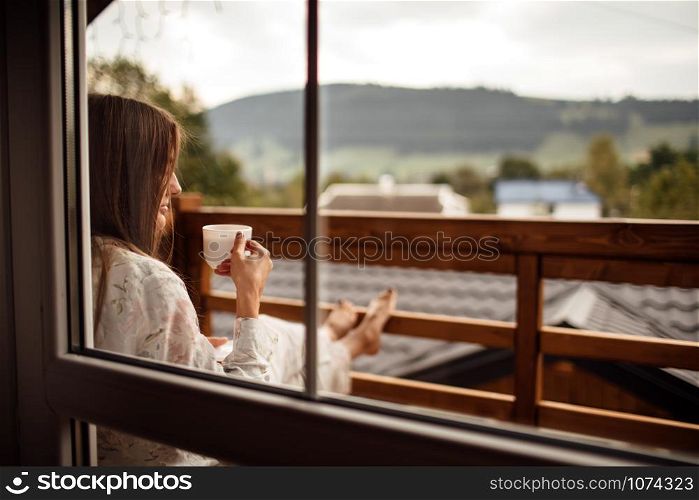 Young woman on the balcony holding a cup of coffee ore tea in the morning. She in hotel room looking at the nature in sumer. Girl is dressed in stylish nightwear. Relax time. Young woman on the balcony holding a cup of coffee ore tea in the morning. She in hotel room looking at the nature in sumer. Girl is dressed in stylish nightwear. Relax time.