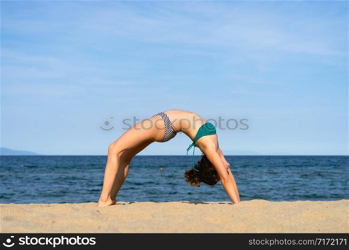 Young woman on the beach practice yoga in bridge position Setu Bandhasana asana by the seaside in sunny day