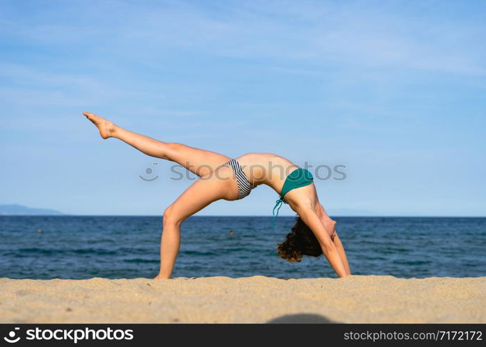 Young woman on the beach practice yoga in bridge position Setu Bandhasana asana by the seaside in sunny day