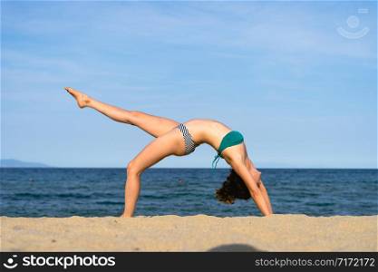 Young woman on the beach practice yoga in bridge position Setu Bandhasana asana by the seaside in sunny day