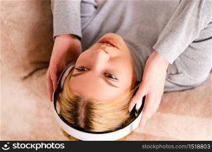 Young woman on the bed lying listen to the music via headphones, enjoying at home