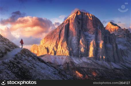 Young woman on the trail looking on high mountain peak at sunset in Dolomites, Italy. Autumn landscape with girl, path, rocks, sky with clouds at colorful sunset. Hiking in alps. Majestic mountains
