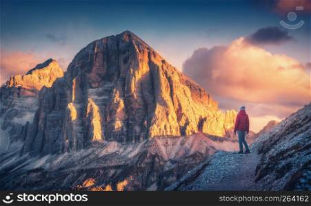 Young woman on the trail looking on high mountain peak at sunset in Dolomites, Italy. Autumn landscape with girl, path, rocks, sky with clouds at colorful sunset. Hiking in alps. Majestic mountains