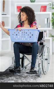 young woman on wheelchair putting laundry into the washing machine
