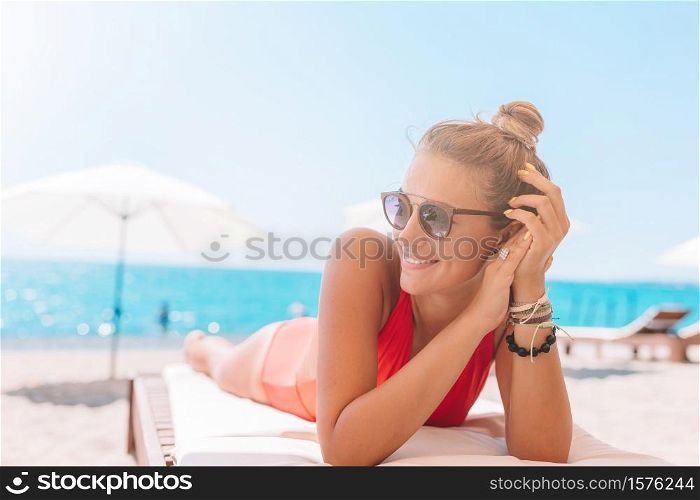 Young woman on white beach sitting on sunbed. Young woman in swimsuit with cocktail glass on white beach sitting on sunbed