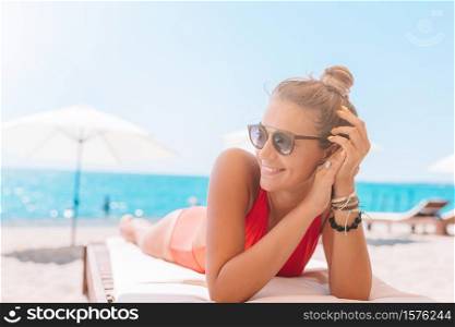 Young woman on white beach sitting on sunbed. Young woman in swimsuit with cocktail glass on white beach sitting on sunbed