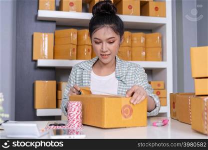 young woman online entrepreneur using tape to packing parcel box at home office, prepare product for deliver to customer.