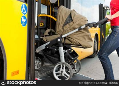 Young woman - only torso - with a baby in a stroller getting into a bus on the bus station