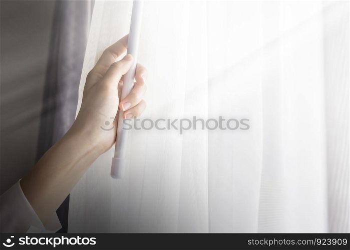 Young woman opening curtains in bedroom
