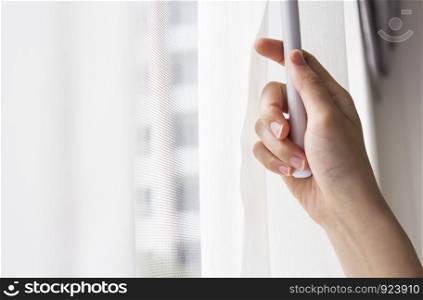 Young woman opening curtains in bedroom