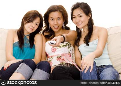 Young woman operating a remote control with two young women sitting beside her on a couch
