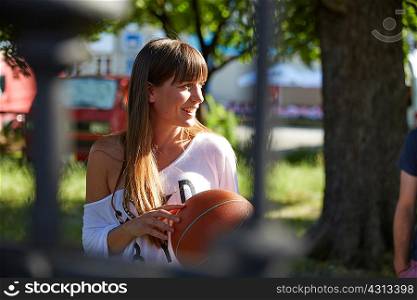 Young woman outdoors, holding basketball, smiling
