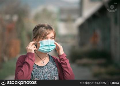 Young woman outdoors putting on face mask. Corona and flu season.