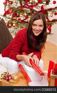 Young woman packing Christmas present in front of tree