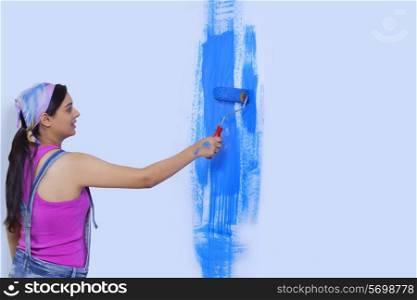 Young woman painting her home wall