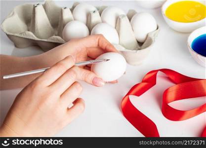 Young woman paints white eggs for Easter. A young woman is painting on Easter eggs on a white background. The egg in the girl’s hand. Young woman paints white eggs for easter.