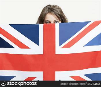 Young woman peeking over British flag against gray background