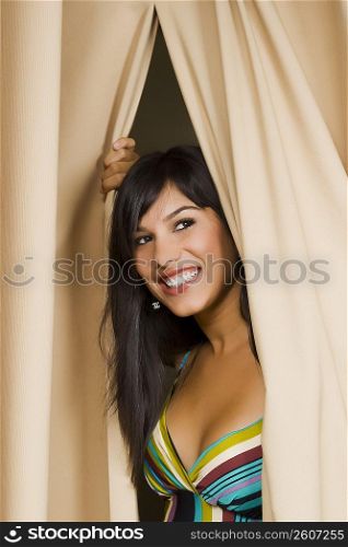 Young woman peeking through a curtain and smiling