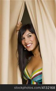 Young woman peeking through a curtain and smiling