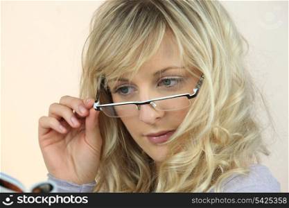 Young woman peering over her glasses at a magazine