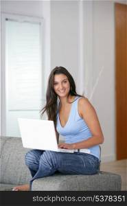 Young woman perched on a sofa with a laptop