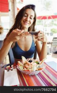 Young woman photographing her salad with a smartphone while sitting in a coastal restaurant. Young woman photographing her salad with a smartphone while sitting in a restaurant