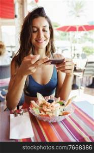 Young woman photographing her salad with a smartphone while sitting in a coastal restaurant. Young woman photographing her salad with a smartphone while sitting in a restaurant